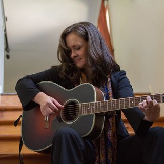 A woman sitting on the steps playing an acoustic guitar.